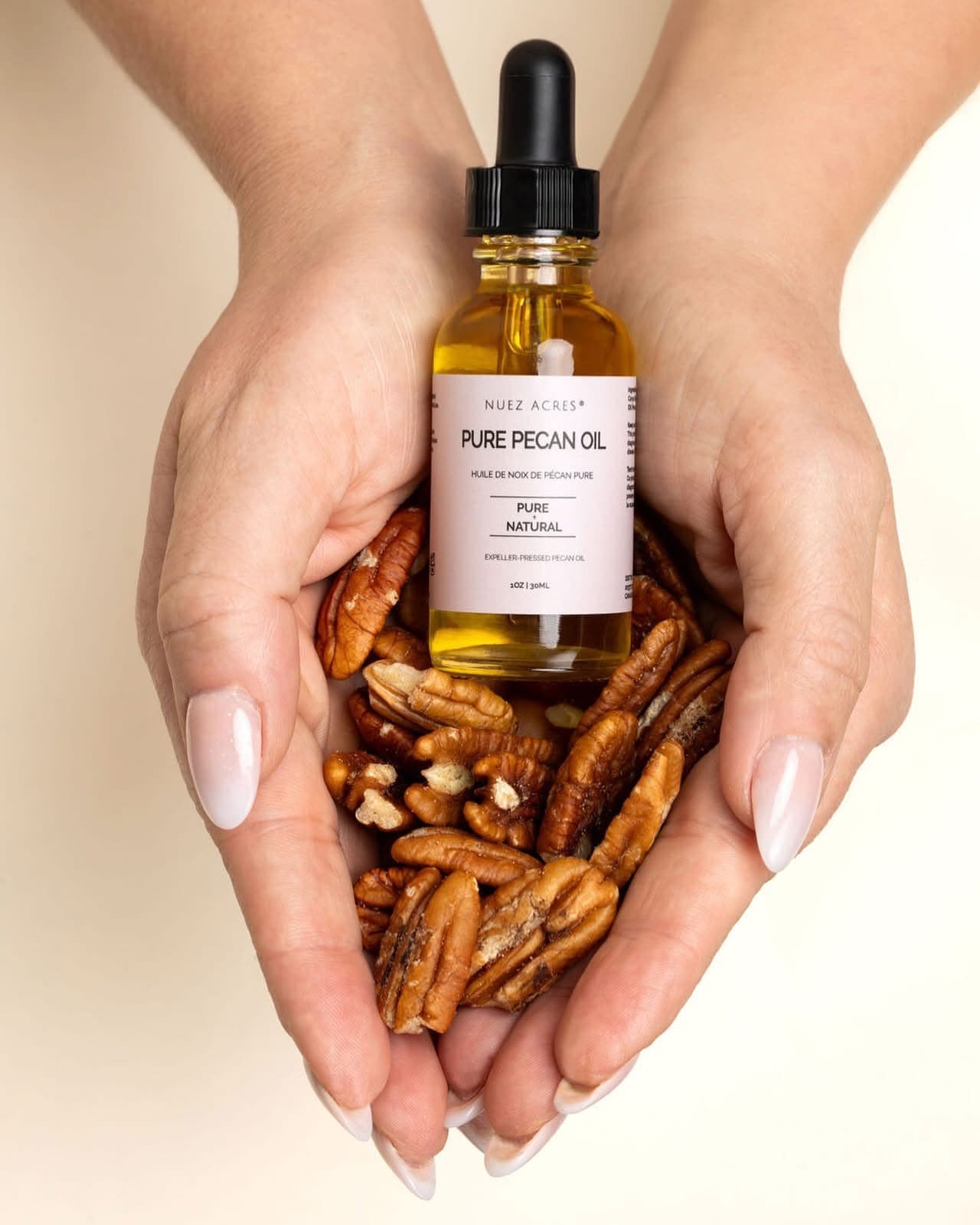 Nuez Acres Pure Pecan Oil product bottle surrounded by pecans held in two hands